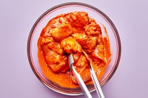 chicken thighs being tossed in red pepper sauce marinade