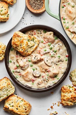 a bowl of Chicken à la King made with chicken, mushrooms and peas in a creamy white sauce served with onion chive biscuits