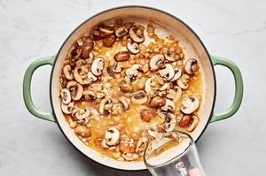 white wine being poured in a skillet with mushrooms, onion, garlic and butter