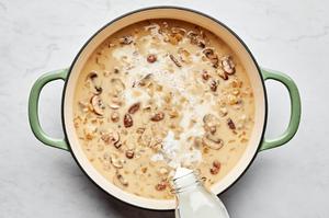 whole milk and spices being added to a skillet with chicken broth, white wine, flour, mushrooms, onion, garlic and butter