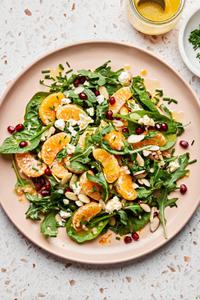 Christmas Salad on a platter made with spinach, arugula, feta, clementines, pomegranates, almond, chives and citrus dressing