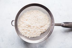 long grain white rice being rinsed in a fine mesh sieve