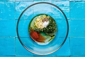 olive oil, garlic, honey, lime zest, lime juice, cilantro, chili powder, salt, and pepper being combined in a glass bowl