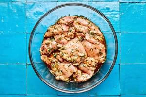 chicken thighs being tossed with olive oil, garlic, honey, lime zest, lime juice, cilantro, chili powder, salt, and pepper