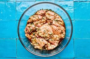 chicken thighs being tossed with olive oil, garlic, honey, lime zest, lime juice, cilantro, chili powder, salt, and pepper