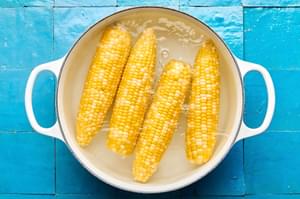 corn on the cob being boiled in a pot of hot water