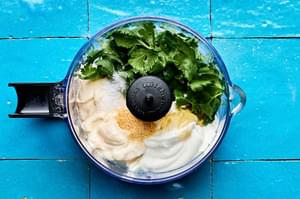mayonnaise, sour cream, lime juice, honey, cilantro leaves, garlic powder, and salt being combined in a food processor