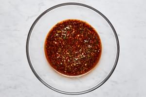 Marinade made with olive oil, garlic, honey, lime zest, lime juice, cilantro, chili powder, salt, and pepper in a glass bowl