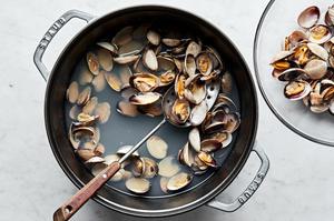 clams that have been cooked in boiling water in a pot and being transferred to a bowl with a slotted spoon