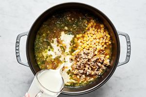 corn, heavy cream and clam meat being added to a large pot of clam chowder