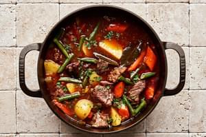 a pot of homemade classic beef stew with potatoes, green beans and carrots sprinkled with fresh parsley