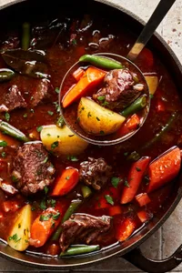 classic beef stew with potatoes, carrots and green beans being scooped out of a pot with a ladle
