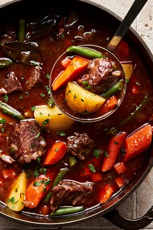 classic beef stew with potatoes, carrots and green beans being scooped out of a pot with a ladle