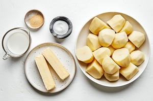 peeled russet potatoes, butter, whole milk, salt and garlic powder in prep bowls to make classic mashed potatoes