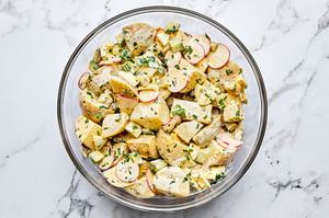 a bowl of homemade classic potato salad made with chives, parsley, cucumbers, pickles, eggs and radishes