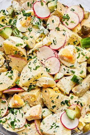a bowl of homemade classic potato salad made with chives, parsley, cucumbers, pickles, eggs and radishes