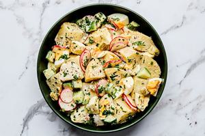a bowl of homemade classic potato salad made with chives, parsley, cucumbers, pickles, eggs and radishes