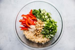 ingredients in a bowl for cold ramen noodle salad green onions, red bell pepper, peanuts, cucumbers, basil, cilantro.