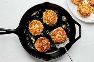 homemade corn fritters being fried in butter and oil in a skillet