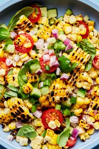 corn salad made with tomatoes, cucumber, red onion, green onions, basil and lime juice in a serving bowl with a spoon