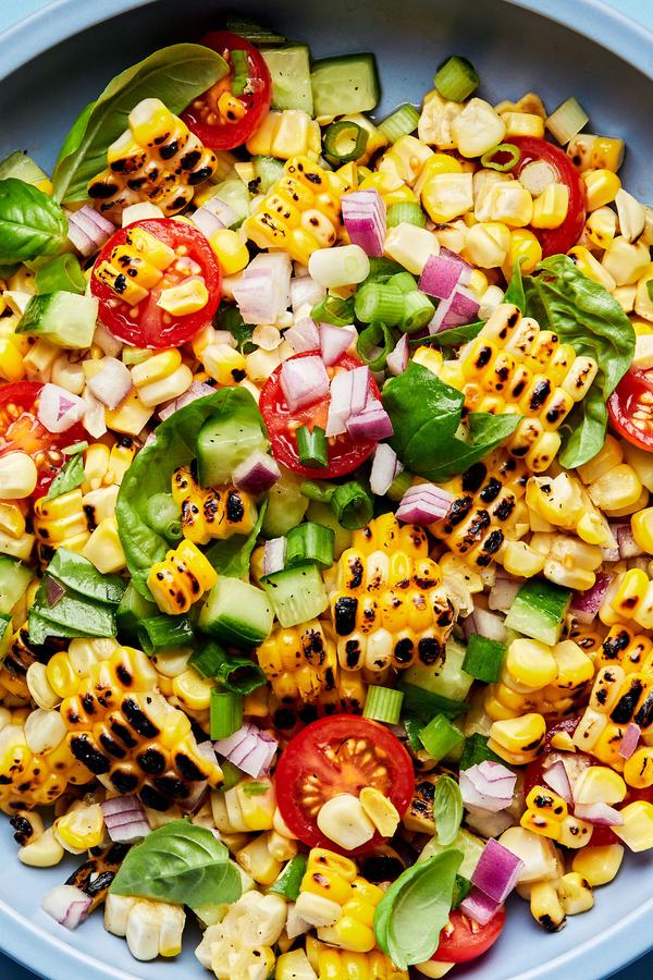 corn salad made with tomatoes, cucumber, red onion, green onions, basil and lime juice in a serving bowl with a spoon