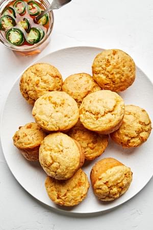 A pile of 11 cornbread muffins next to a jar of Jalapeño-infused honey