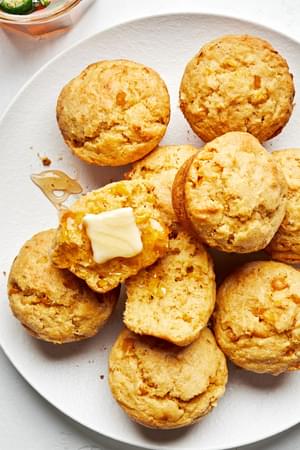 A pile homemade cornbread muffins on a plate, drizzled with jalapeño-infused honey