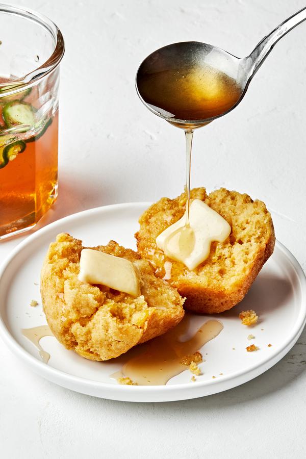 A buttered cornbread muffin being drizzled with jalapeño-infused honey