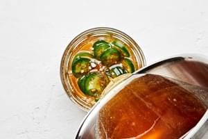 warmed honey being poured into a jar containing sliced jalapeño peppers to make jalapeño infused honey