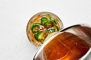 warmed honey being poured into a jar containing sliced jalapeño peppers to make jalapeño infused honey