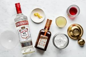 ingredients laid out to make a cosmopolitan cocktail: vodka, cointreau, cranberry juice, lime juice and lemon twists
