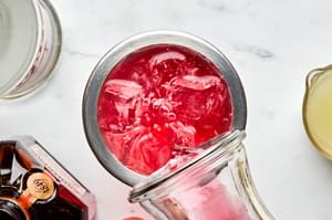 vodka, cointreau and cranberry juice added to a cocktail to make a cosmopolitan cocktail