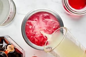 vodka, cointreau, cranberry juice and lime juice added to a cocktail to make a cosmopolitan cocktail