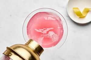 a homemade cosmopolitan being poured into a martini glass