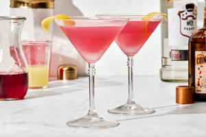 2 homemade Cosmopolitan cocktails with a twist of lemon, served in  classic martini glasses.