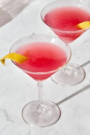 2 homemade Cosmopolitan cocktails with a twist of lemon, served in  classic martini glasses.
