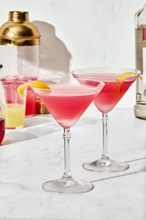 2 homemade Cosmopolitan cocktails with a twist of lemon, served in  classic martini glasses.