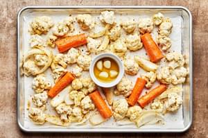 cauliflower, carrots & onion tossed with olive oil, nutritional yeast,  salt & pepper and a dish of garlic on a baking sheet
