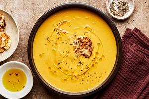 a bowl of cream of cauliflower soup topped with garlic oil & pepper surrounded by bowls of extra pepper and garlic oil