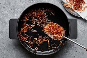 fried shallots in a large pot being scooped out with a spoon onto a paper towel lined plate