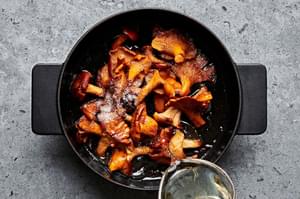 white wine being poured into a pot of mushrooms that have been cooked in olive oil and butter