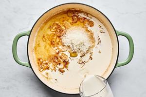 cream being poured into a skillet with shallot, garlic, chicken stock, bouillon, Parmesan and salt