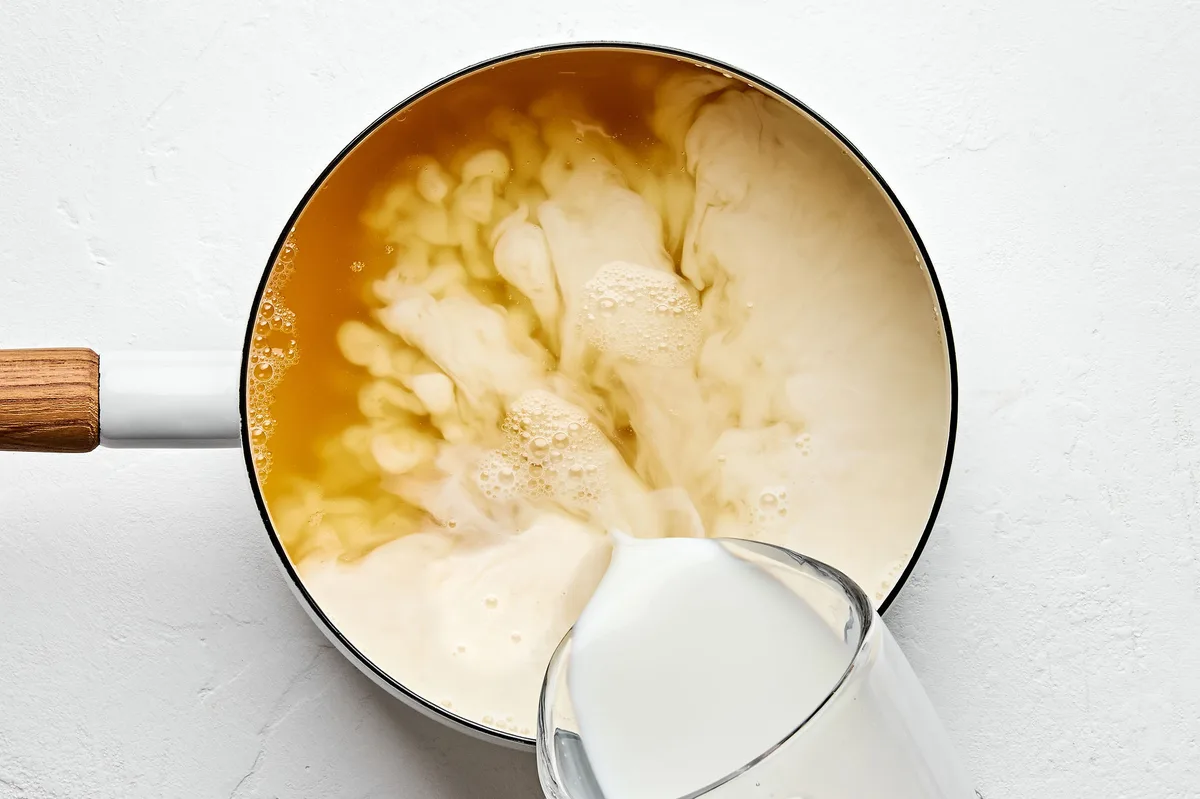 chicken stock and whole milk being poured into a sauce pan