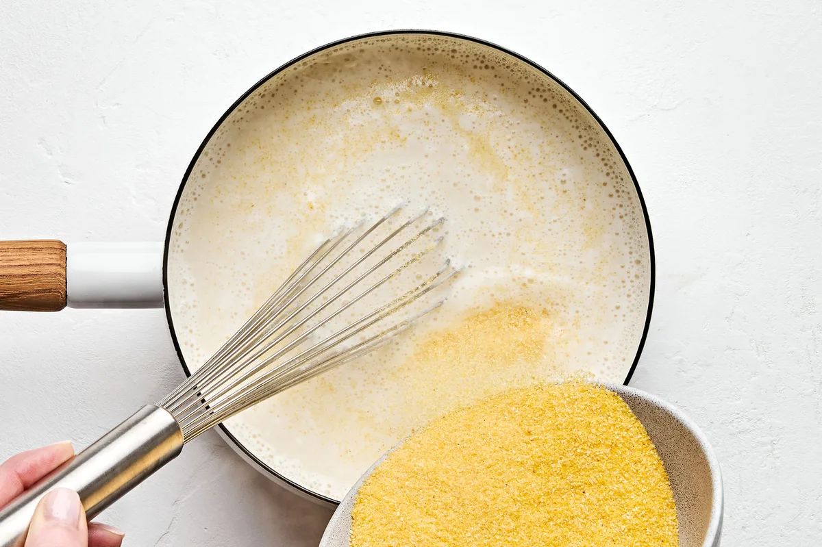ground polenta being whisked into a sauce pan with chicken stock and milk