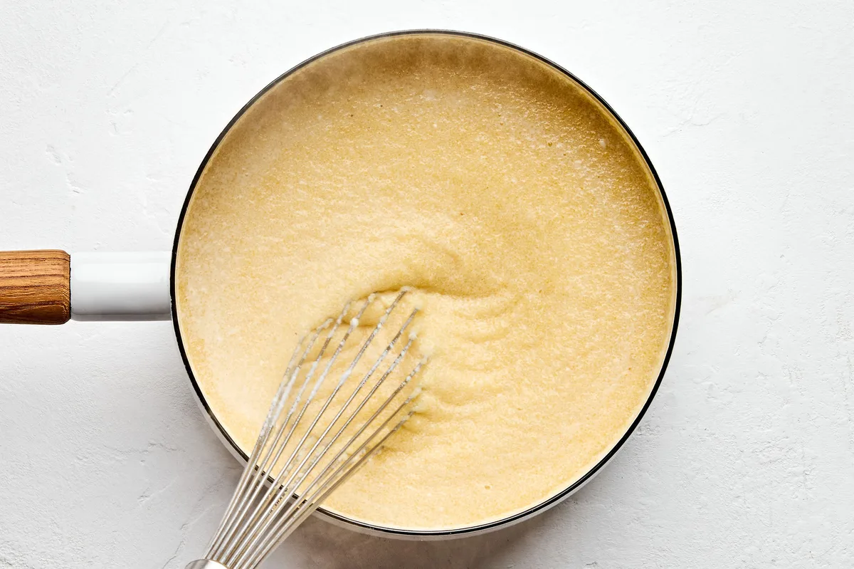 chicken stock, milk and ground polenta being whisked together in a sauce pan