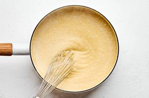 chicken stock, milk and ground polenta being whisked together in a sauce pan