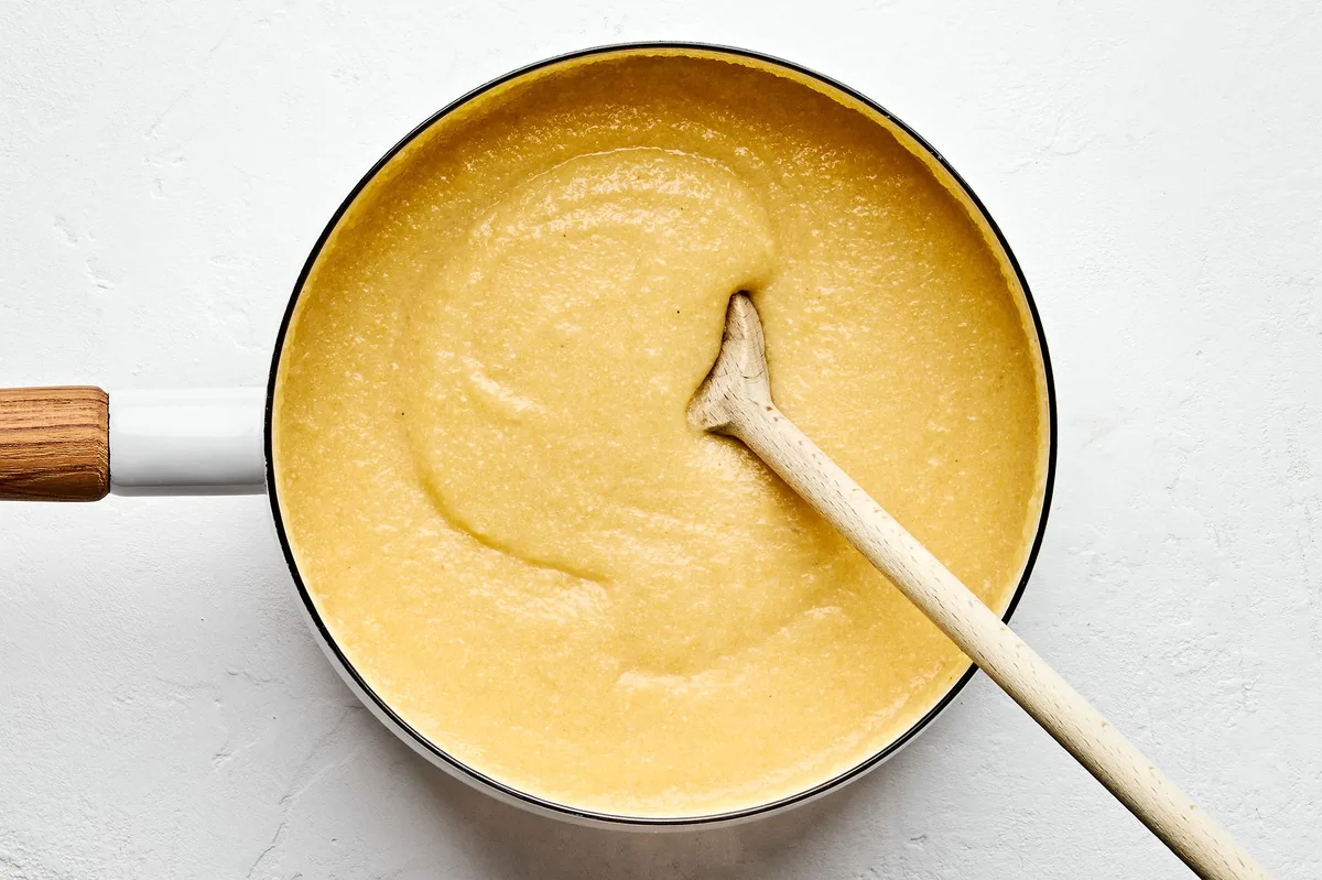 homemade polenta thickening in a sauce pan being stirred with a wooden spoon