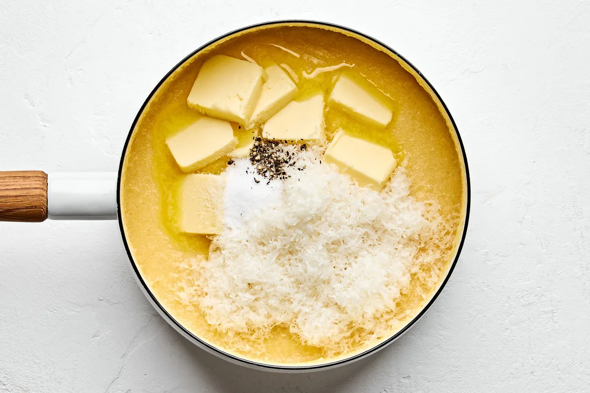 butter, Parmesan, salt and pepper being added to a sauce pan with chicken stock, milk and polenta