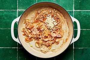 sliced shallots and minced garlic in a large white skillet on green tiled background