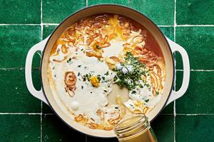 heavy cream and chicken stock being poured into a white skillet with tarragon and shallots.